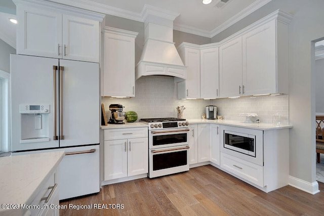 kitchen with white cabinetry, built in appliances, light wood-type flooring, and wall chimney exhaust hood