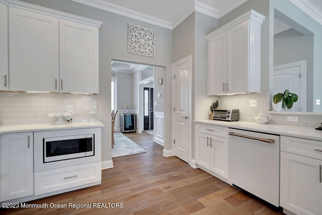 kitchen with built in microwave, white cabinetry, ornamental molding, white dishwasher, and light hardwood / wood-style flooring