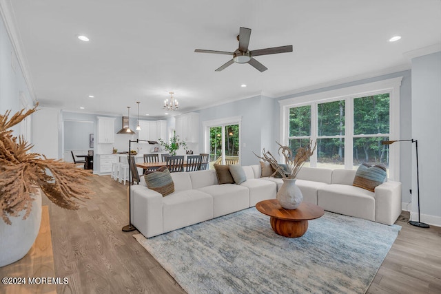 living room featuring crown molding, light wood-type flooring, and ceiling fan with notable chandelier