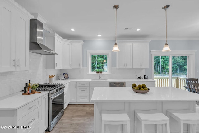 kitchen featuring wall chimney range hood, white cabinetry, appliances with stainless steel finishes, and a wealth of natural light