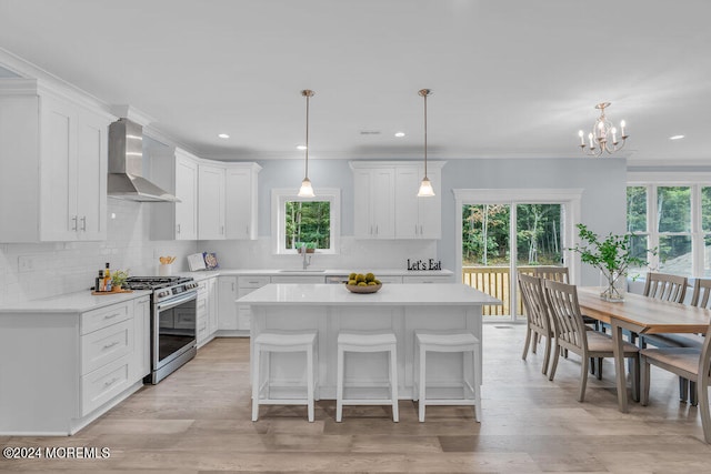 kitchen with wall chimney range hood, hanging light fixtures, white cabinetry, a center island, and stainless steel gas range