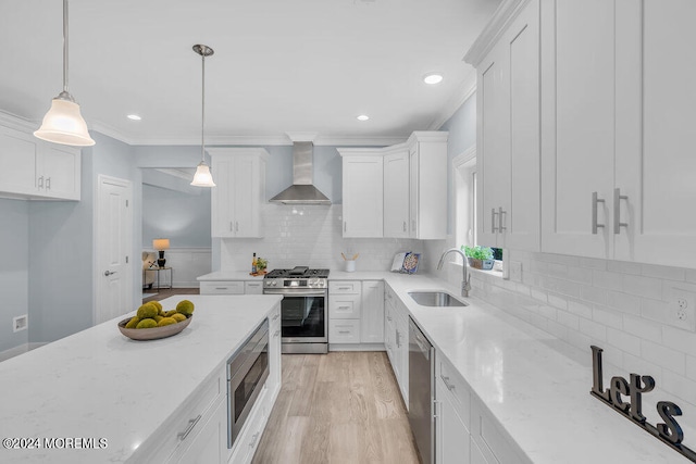 kitchen featuring wall chimney range hood, appliances with stainless steel finishes, white cabinetry, sink, and decorative light fixtures