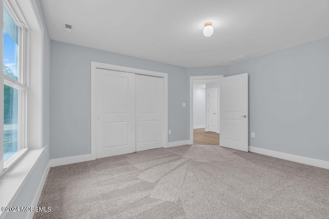 unfurnished bedroom with multiple windows, a closet, and light colored carpet