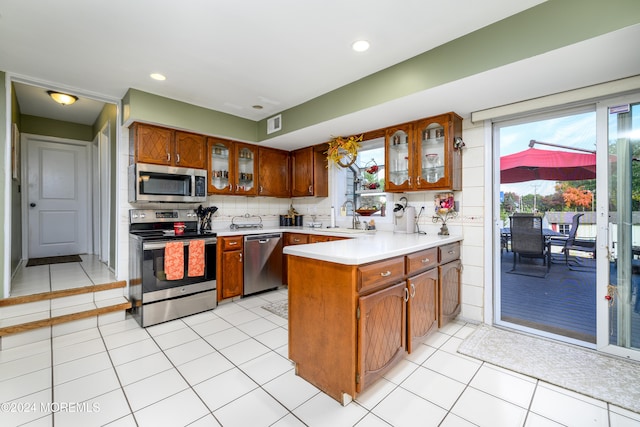 kitchen featuring kitchen peninsula, stainless steel appliances, sink, light tile patterned flooring, and tasteful backsplash