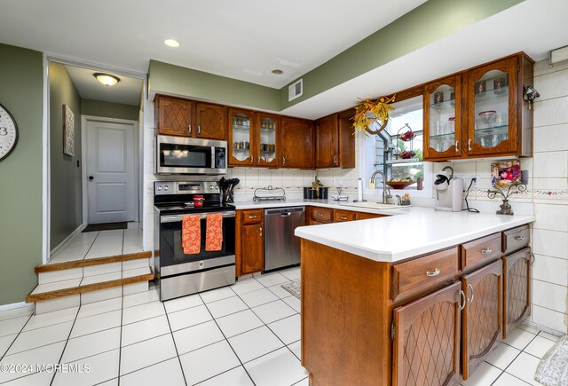 kitchen with decorative backsplash, kitchen peninsula, sink, light tile patterned floors, and appliances with stainless steel finishes