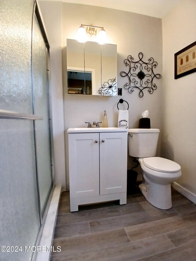 bathroom featuring a shower with door, toilet, vanity, and wood-type flooring