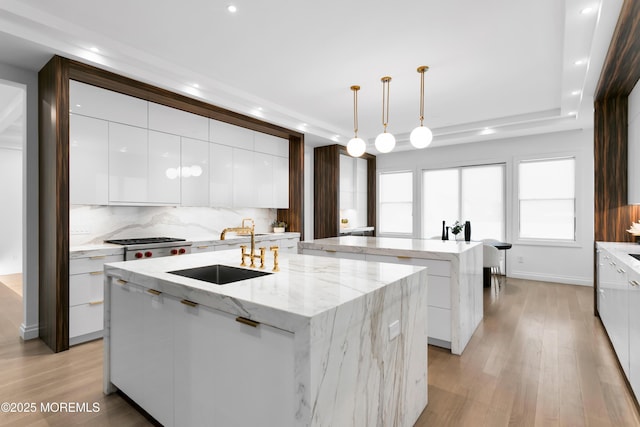 kitchen featuring backsplash, sink, decorative light fixtures, white cabinetry, and an island with sink