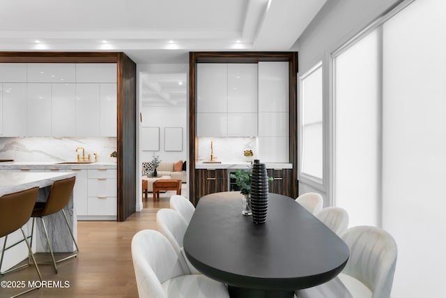 dining area featuring beamed ceiling, light hardwood / wood-style flooring, and sink