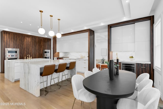 kitchen with a kitchen island with sink, pendant lighting, decorative backsplash, dark brown cabinets, and light wood-type flooring