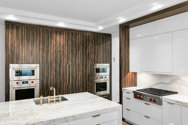 kitchen featuring light stone counters, stainless steel appliances, white cabinetry, and sink