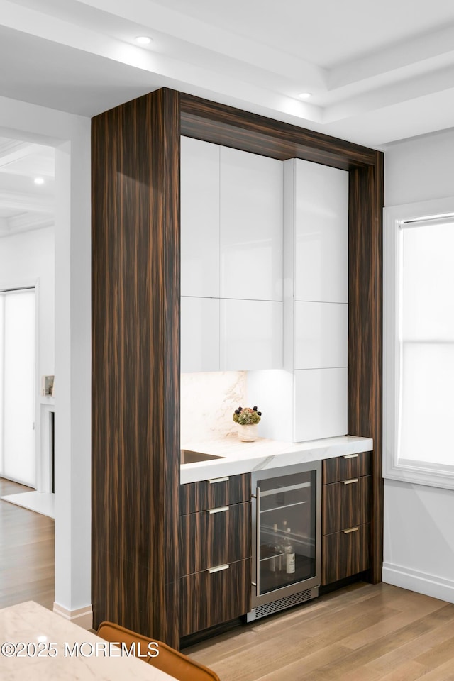 bar with dark brown cabinets, light wood-type flooring, and beverage cooler