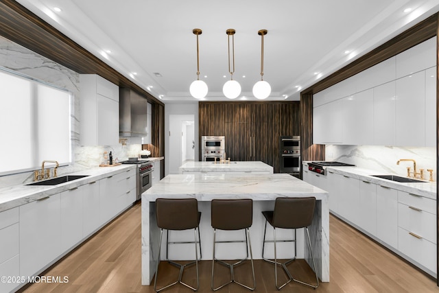 kitchen featuring sink, appliances with stainless steel finishes, a center island, and wall chimney range hood