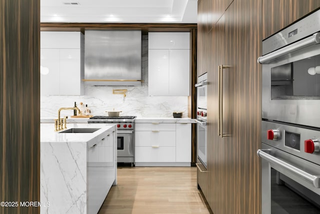 kitchen featuring sink, wall chimney exhaust hood, stainless steel appliances, white cabinets, and light wood-type flooring