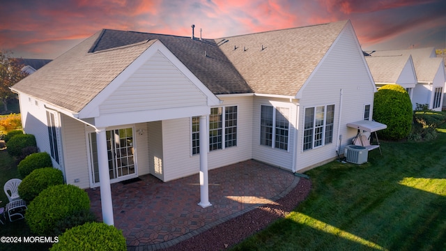 back house at dusk with a patio, a lawn, and central AC unit