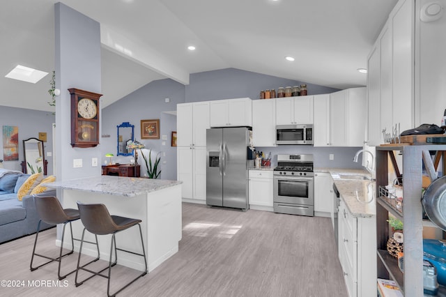 kitchen featuring lofted ceiling with skylight, appliances with stainless steel finishes, light hardwood / wood-style flooring, and white cabinets