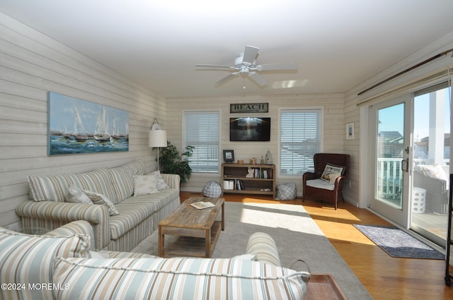 living room featuring light hardwood / wood-style floors, wood walls, and ceiling fan