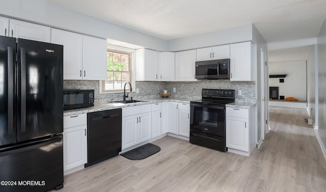 kitchen with white cabinetry, light stone countertops, light hardwood / wood-style flooring, black appliances, and sink