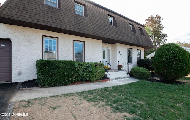 view of front of house featuring a shingled roof, a front lawn, stucco siding, and mansard roof