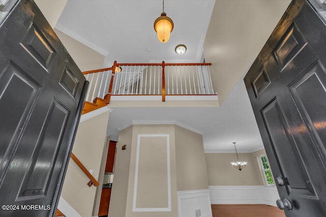 stairway with a towering ceiling, a notable chandelier, ornamental molding, and hardwood / wood-style floors