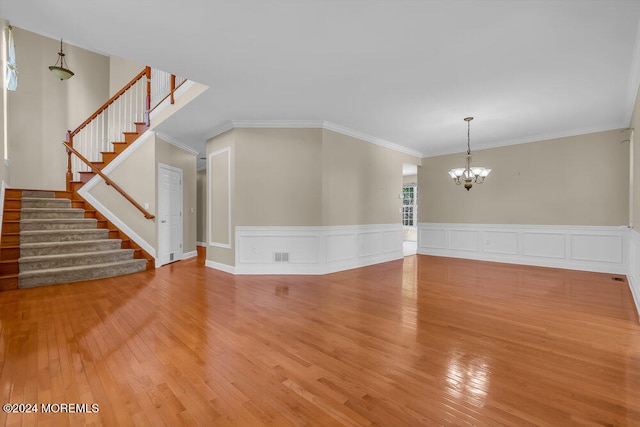 unfurnished living room featuring ornamental molding, wood-type flooring, and an inviting chandelier