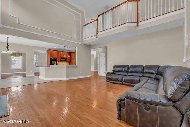 living room with ornamental molding, a high ceiling, light wood-type flooring, and an inviting chandelier