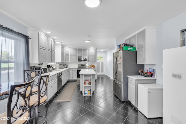 kitchen with tasteful backsplash, appliances with stainless steel finishes, dark tile patterned floors, sink, and a center island