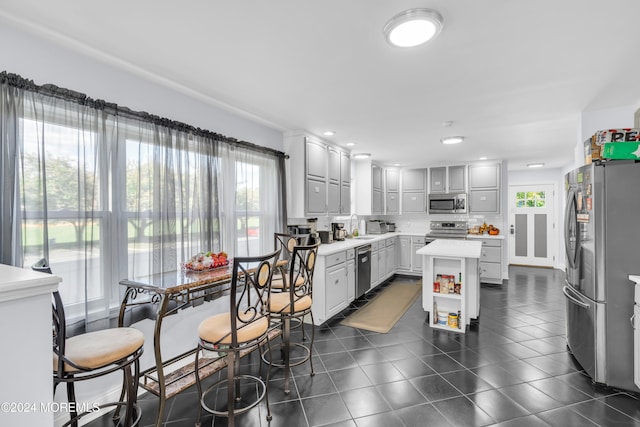 kitchen with dark tile patterned flooring, sink, a center island, stainless steel appliances, and decorative backsplash