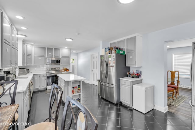 kitchen featuring gray cabinetry, dark tile patterned flooring, tasteful backsplash, appliances with stainless steel finishes, and a kitchen island