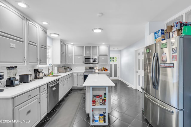 kitchen with backsplash, stainless steel appliances, sink, gray cabinets, and a center island