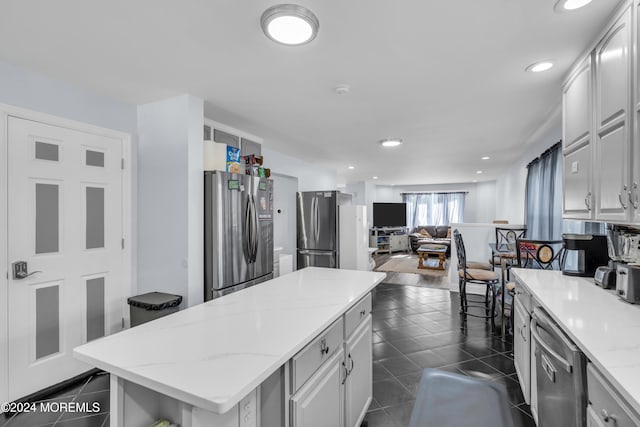 kitchen with a kitchen island, dark tile patterned flooring, stainless steel appliances, light stone countertops, and white cabinetry