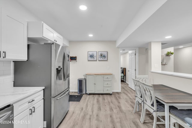 kitchen featuring tasteful backsplash, appliances with stainless steel finishes, white cabinetry, light stone countertops, and light hardwood / wood-style floors