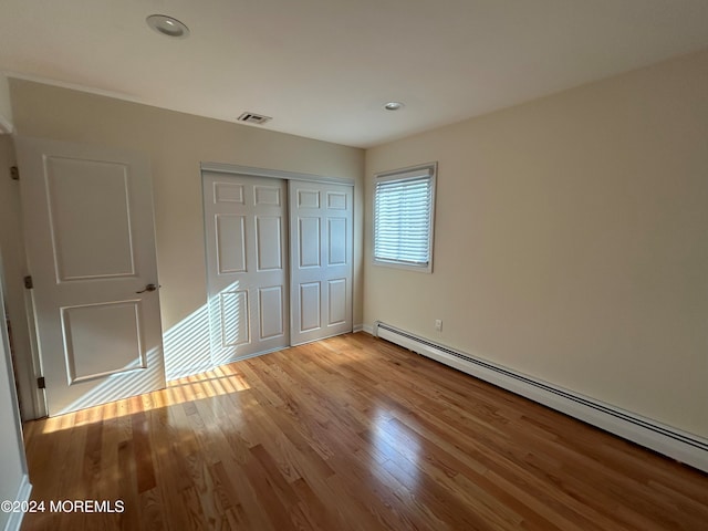 unfurnished bedroom featuring a baseboard radiator, light wood-type flooring, and a closet