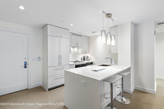 kitchen featuring kitchen peninsula, a breakfast bar, light hardwood / wood-style flooring, sink, and decorative light fixtures