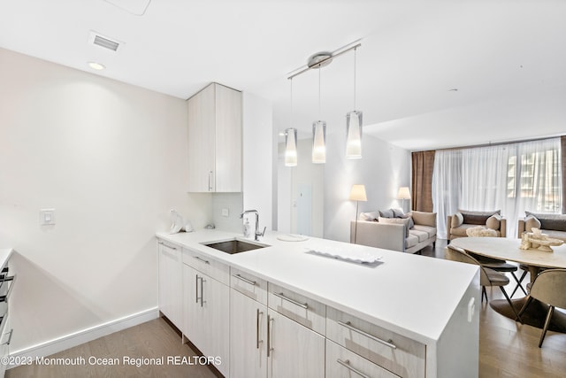 kitchen with kitchen peninsula, hardwood / wood-style flooring, sink, and pendant lighting