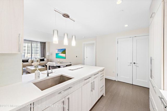 kitchen with decorative backsplash, light hardwood / wood-style flooring, sink, decorative light fixtures, and white cabinetry