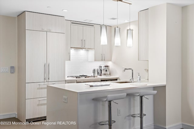 kitchen with decorative backsplash, hanging light fixtures, kitchen peninsula, a kitchen bar, and stainless steel gas stovetop