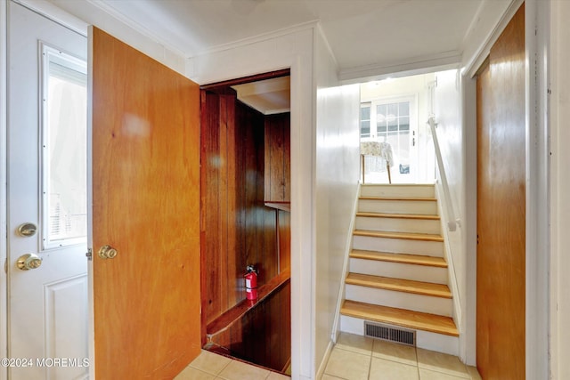 stairway with crown molding, tile patterned floors, and plenty of natural light