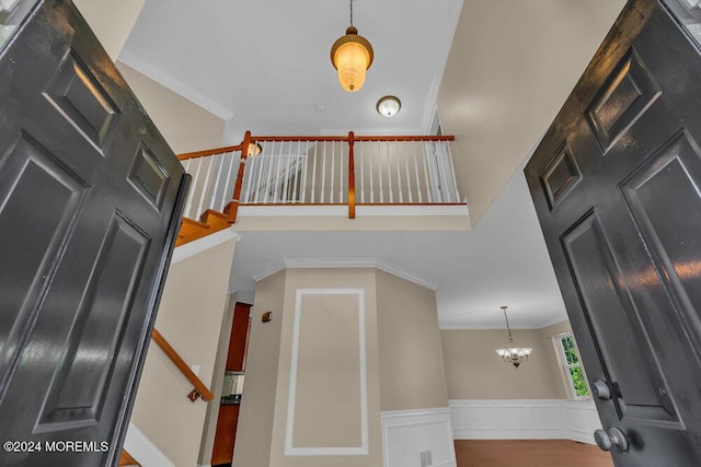 staircase with a decorative wall, a towering ceiling, ornamental molding, wainscoting, and an inviting chandelier