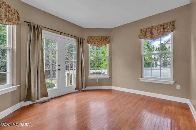 empty room with a wealth of natural light, french doors, light wood-type flooring, and visible vents