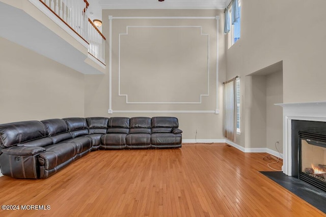 unfurnished living room featuring a fireplace with flush hearth, a towering ceiling, baseboards, and hardwood / wood-style flooring