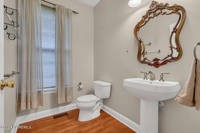 half bathroom with baseboards, visible vents, toilet, wood finished floors, and a sink