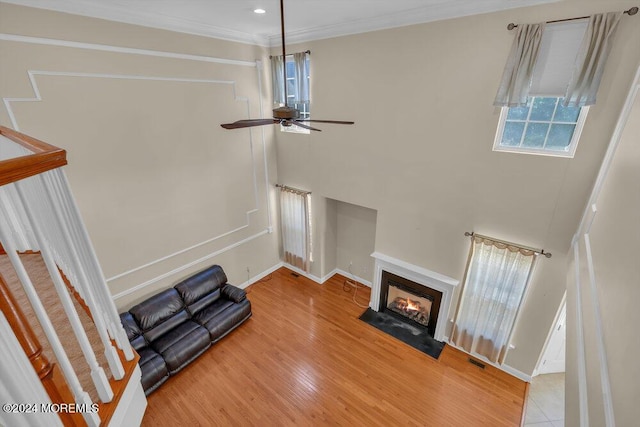 living room with visible vents, a towering ceiling, a fireplace with flush hearth, ornamental molding, and wood finished floors