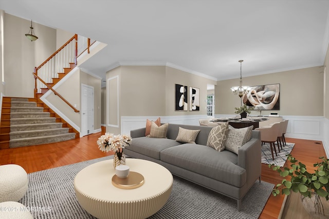 living room with wood finished floors, ornamental molding, stairway, wainscoting, and an inviting chandelier