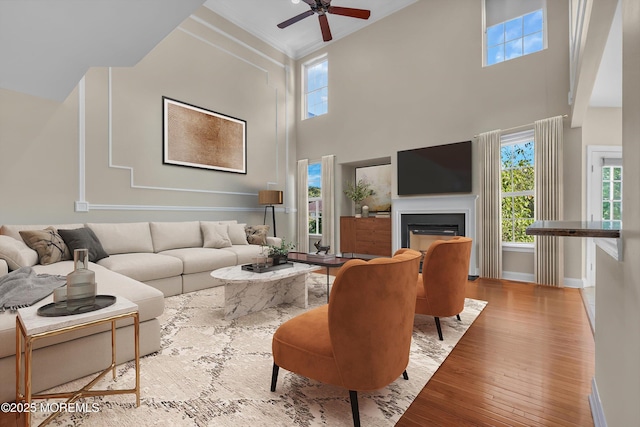 living room featuring a ceiling fan, baseboards, hardwood / wood-style floors, and a glass covered fireplace