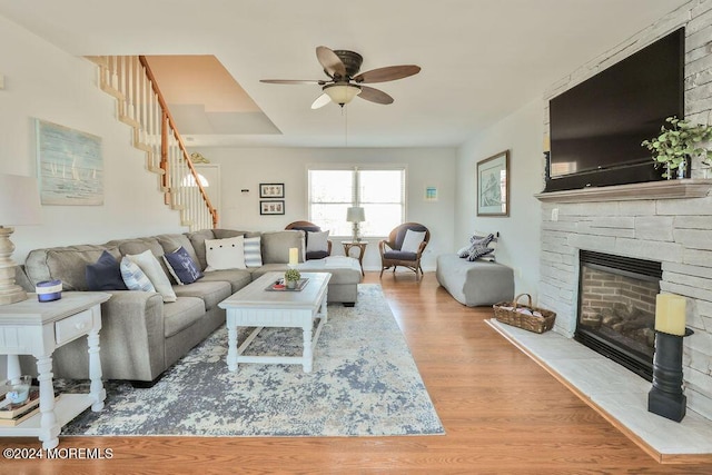 living room featuring stairway, ceiling fan, a stone fireplace, and wood finished floors