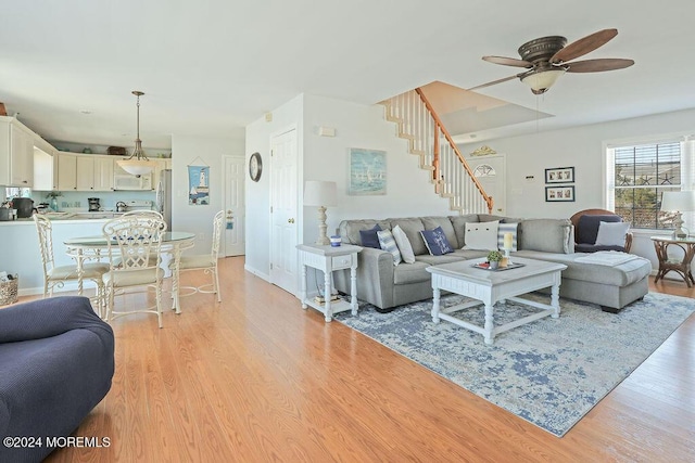 living area featuring a ceiling fan, baseboards, light wood-style flooring, and stairway