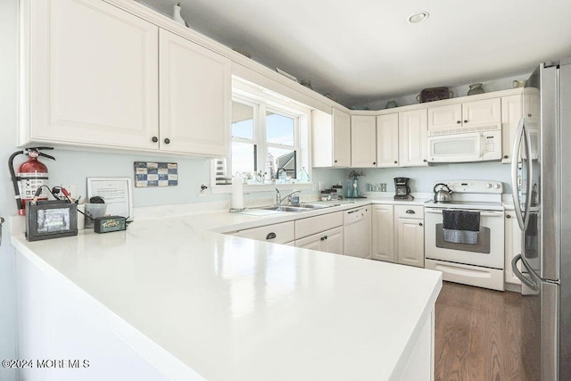 kitchen with dark wood finished floors, light countertops, a sink, white cabinets, and white appliances
