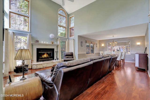 living room with a stone fireplace, high vaulted ceiling, wood-type flooring, and ceiling fan with notable chandelier