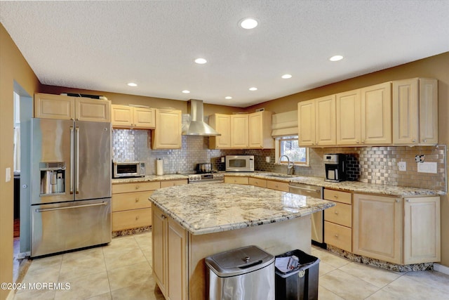 kitchen featuring a center island, light brown cabinets, wall chimney range hood, light tile patterned floors, and appliances with stainless steel finishes