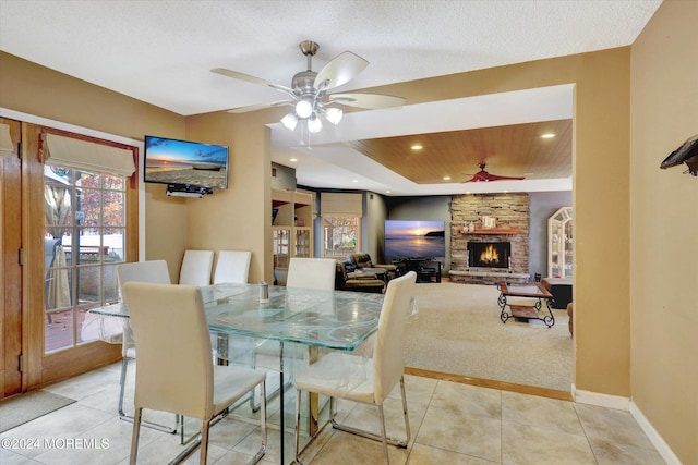 tiled dining room with a textured ceiling, a stone fireplace, and ceiling fan